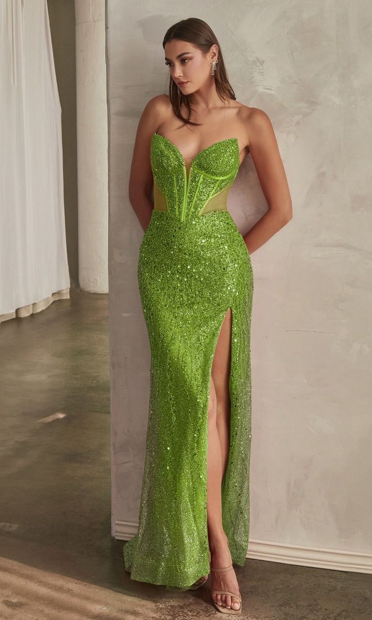 A woman stands against a light wall on a concrete floor wearing the Ladivine CD0227, a strapless long sequin prom dress in bright green with a thigh-high slit.